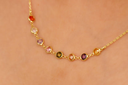 Gold necklace with multicolored gemstones on a person's neck against a beige background