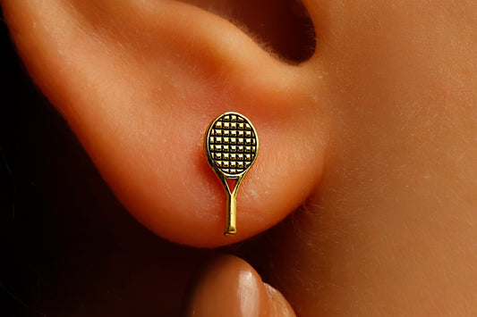 A close-up image of a person's ear wearing a gold-colored tennis racket stud earring.