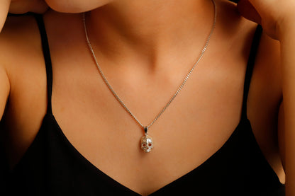 A close-up image of a person wearing a minimalist skull charm necklace with a gold chain and a small skull pendant.