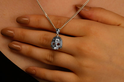 A close-up image of a person wearing a minimalist skull charm necklace with a silver chain and a small skull pendant.