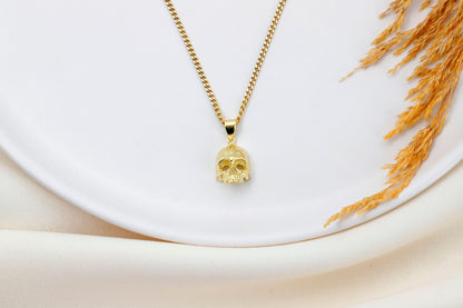 A close-up image of a minimalist skull charm necklace with a gold chain and a small skull pendant.
