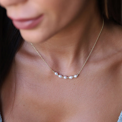 A person wearing a small freshwater beaded pearl necklace in gold tone.