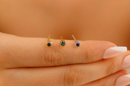 A close-up image of a person's hand holding 3 small stud earrings, with the focus on the earring and the soft earlobe.