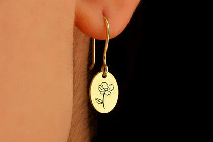 A close-up image of a person wearing a small gold-colored hoop earring with a dangling flower-shaped charm.