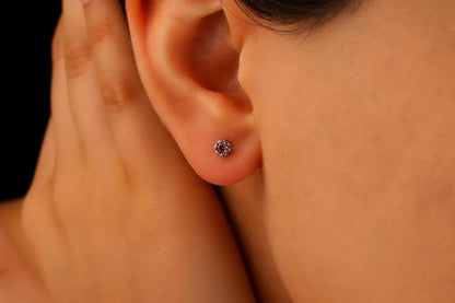 A close-up image of a person's ear wearing a small stud earring, with the focus on the earring and the soft earlobe.