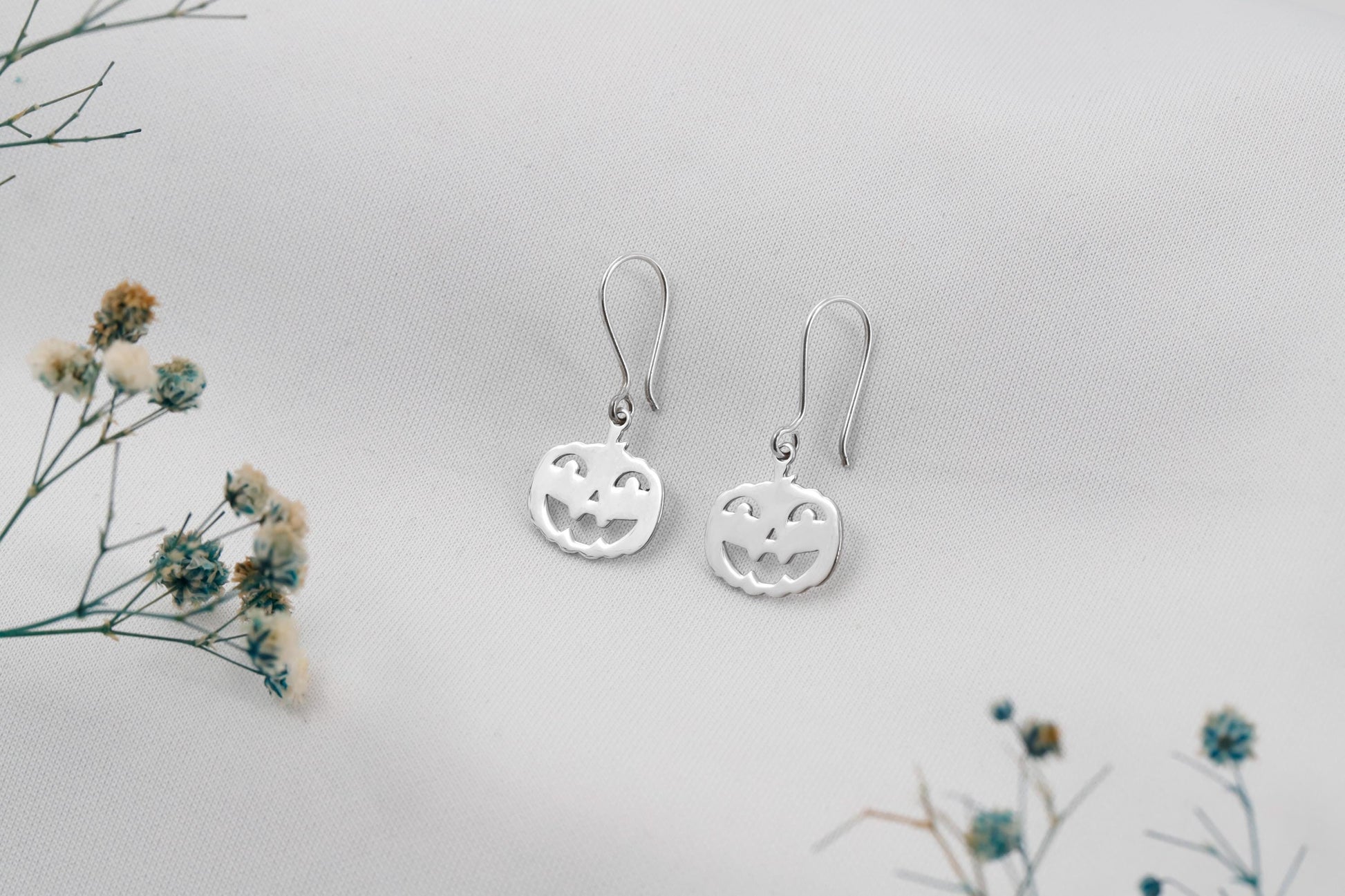 Silver earrings on a light gray background with small flowers.