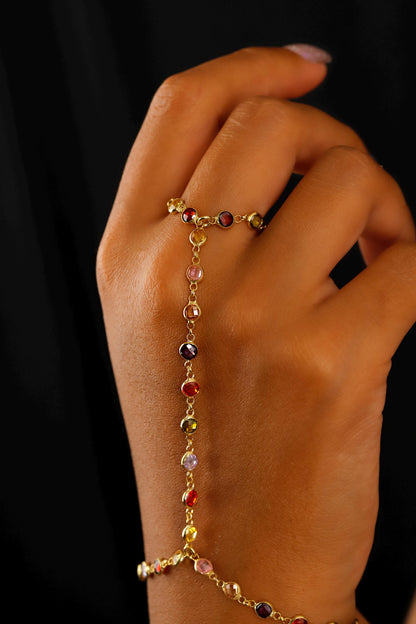 A person wearing a multicolored gemstone hand chain bracelet.