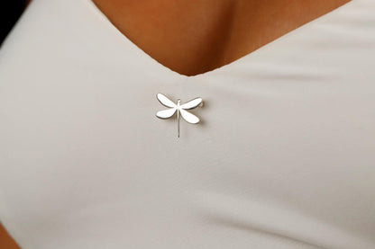 A dainty dragonfly brooch in silver color, attached to a piece of clothing.