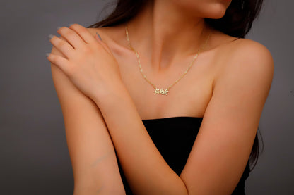 A woman wearing a black dress showcasing a dainty gold-colored necklace with Chinese characters on it.