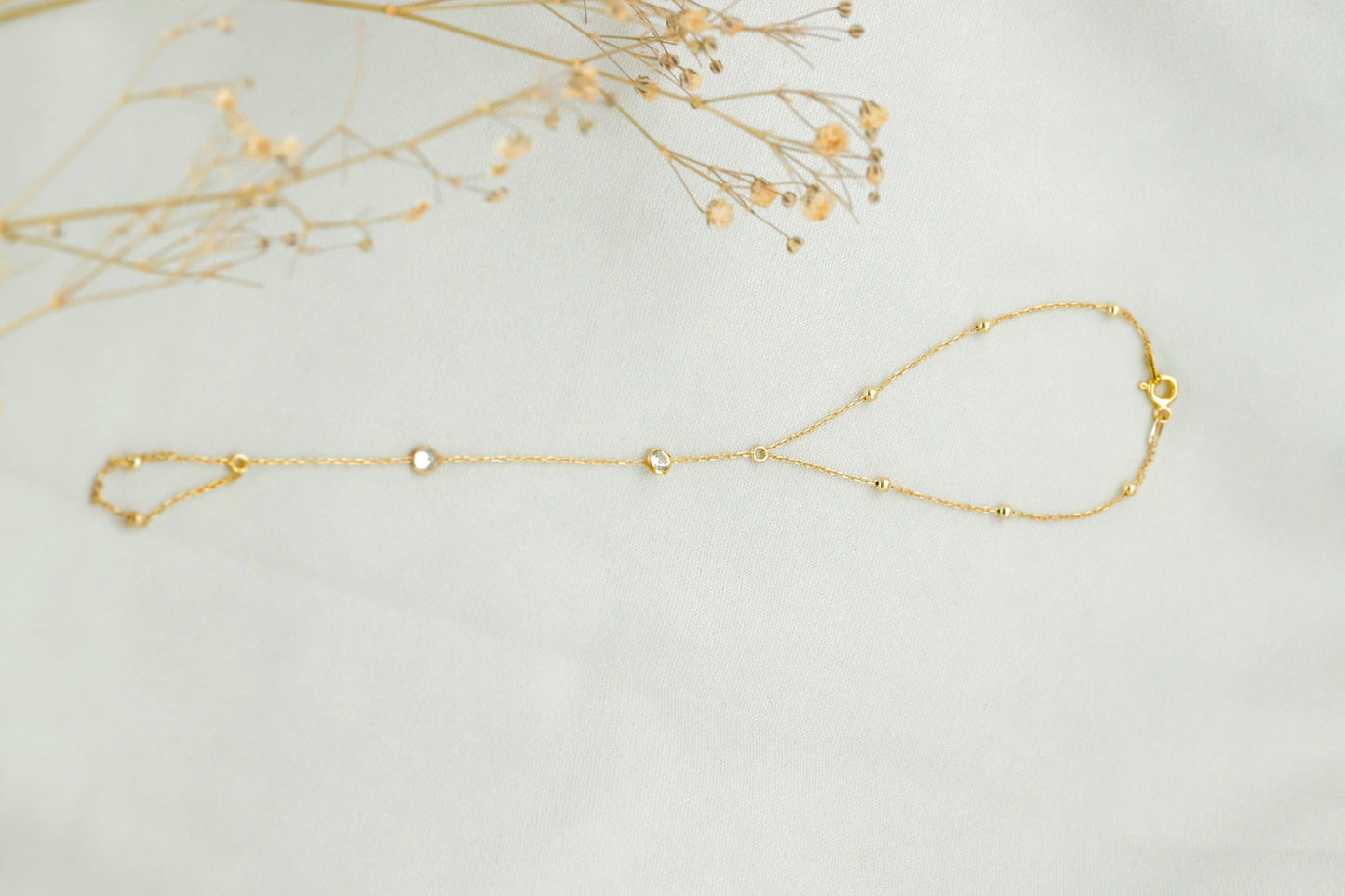 Gold bracelet on a light gray background with dried flowers