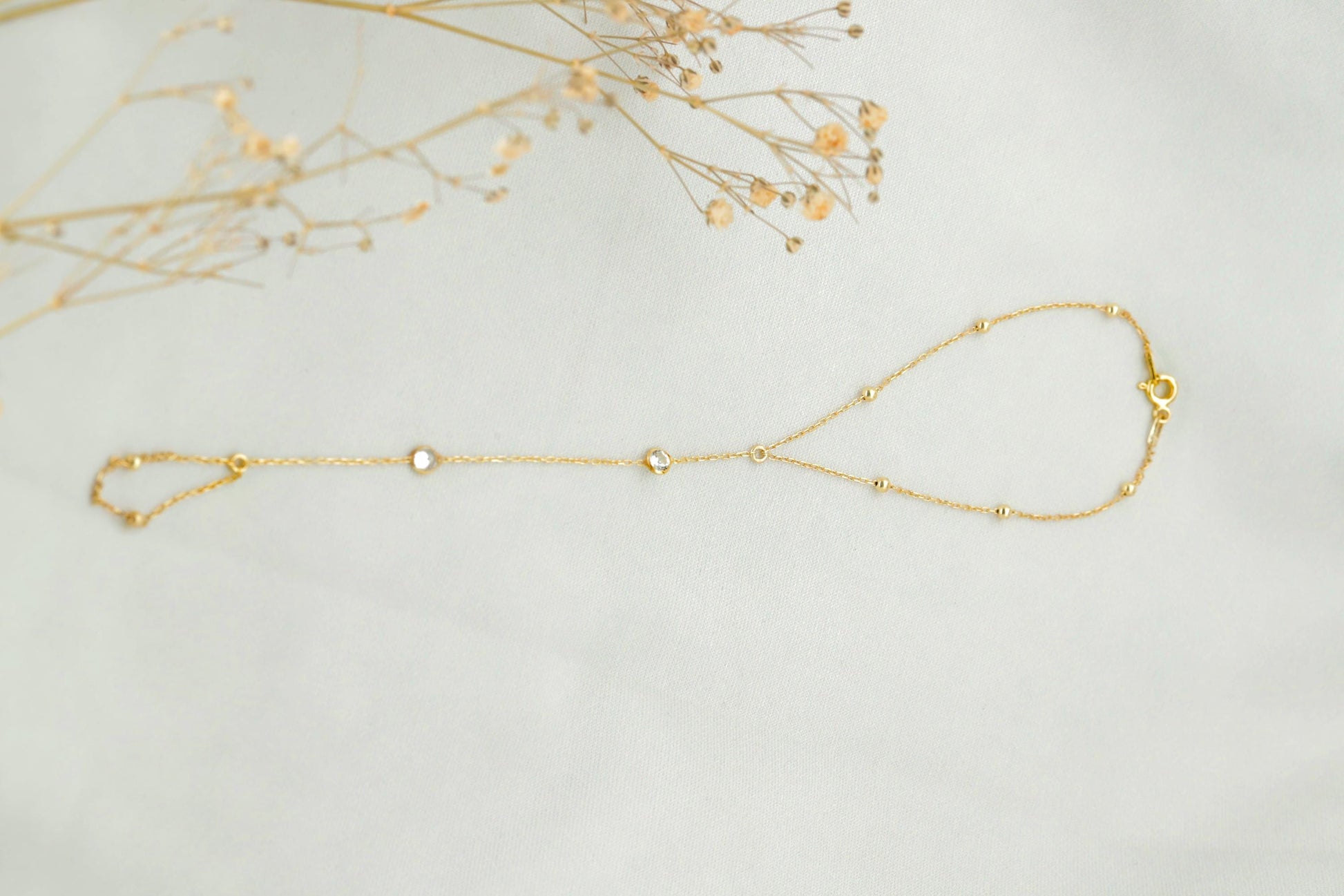 Gold bracelet on a light gray background with dried flowers