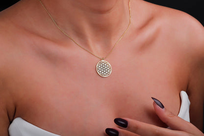 Gold necklace with a circular pendant on a person's neck against a black background