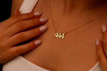A close-up image of a necklace with the number 444 on a charm, held by a person with red nail polish.
