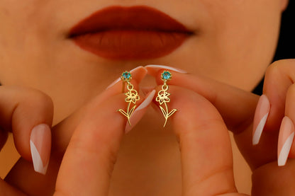 A close-up image of a woman's ear wearing a dangle birth month flower earring with a birthstone.