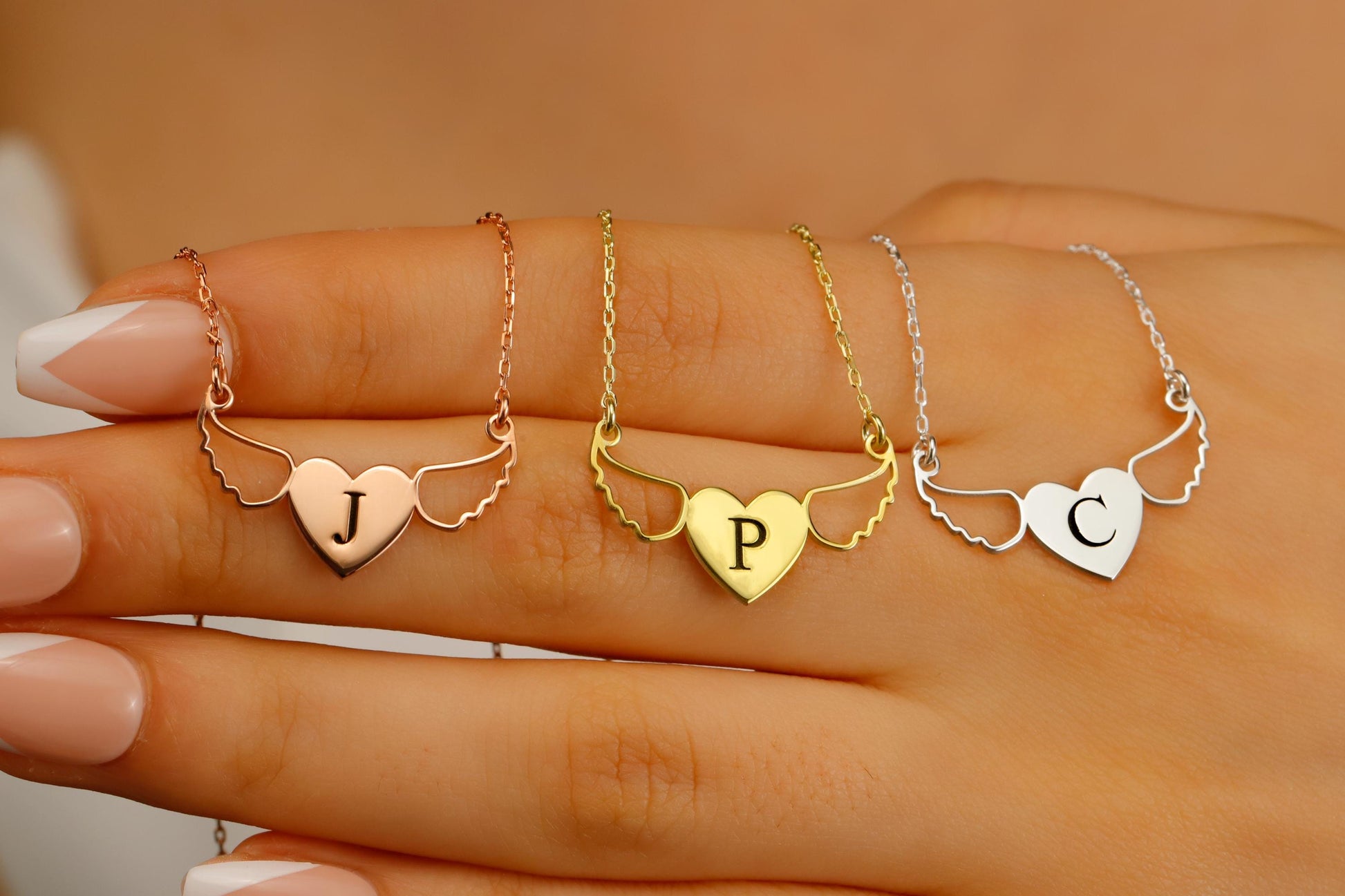 Three heart-shaped necklaces with initials on a hand against a beige background
