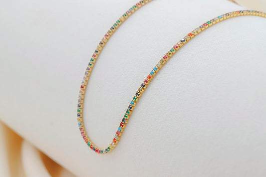 A close-up image of a dainty multicolor necklace with round prong tennis design, featuring colorful CZ stones.
