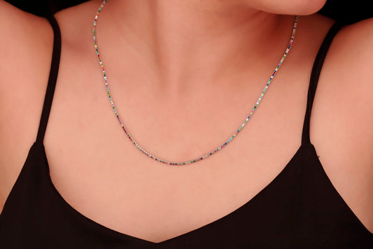 A close-up image of a person wearing a dainty multicolor necklace with round prong tennis design, featuring colorful CZ stones.