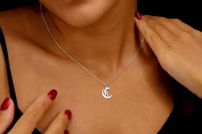 A close-up image of a woman wearing a sterling silver necklace with a gothic style initial pendant.