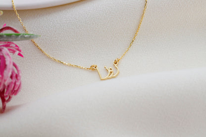 A woman wearing a black tank top showcasing a silver necklace with Arabic script.