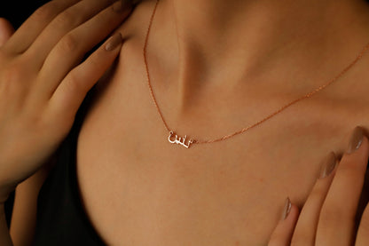 A woman wearing a black tank top showcasing a silver necklace with Arabic script.