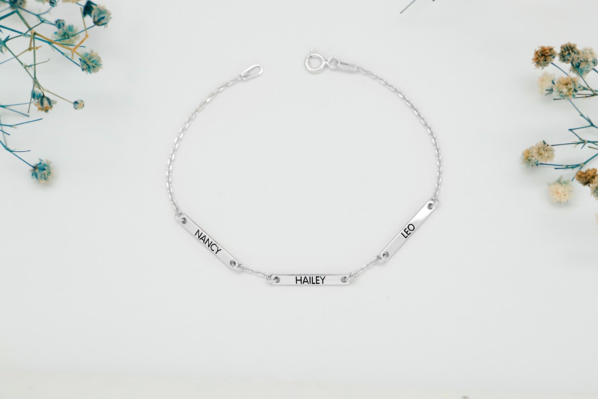 Silver bracelet with engraved names on a white background with flowers