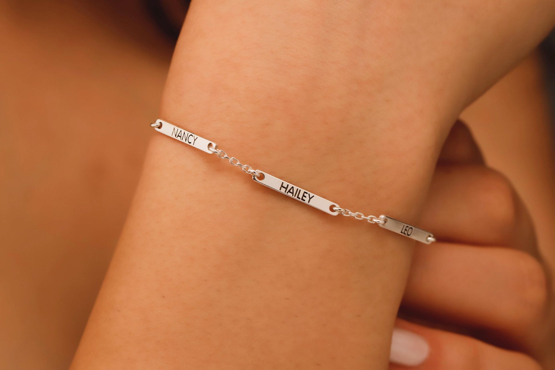 Silver bracelet with engraved names on a wrist against a neutral background