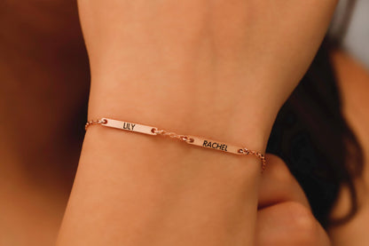 Rose gold bracelet with engraved names on a wrist against a blurred background