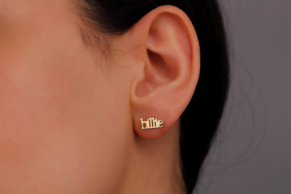A person wearing a pair of gold name earrings with the name 'Billie' inscribed on them.