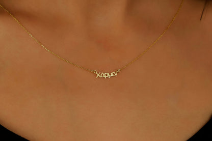 An 18K gold filled name necklace with the name 'Kleo' written in Greek letters, displayed on a person's neck.