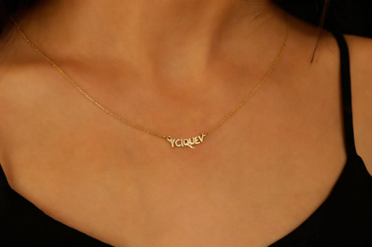 Gold necklace with 'Yoquev' pendant on a person wearing a black top.