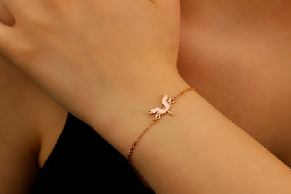A bracelet with a 14K gold charm in the shape of a phoenix bird, displayed on a person's wrist.
