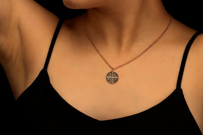 Necklace with a pendant worn by a person against a black background the Christian Eastern Orthodox cross and the initials IC XC NIKA.
