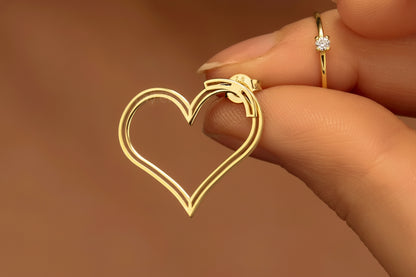 Gold heart-shaped earring held by a hand against a brown background