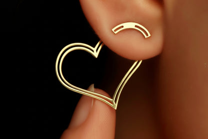 A heart-shaped gold ear jacket earring on a person's ear.