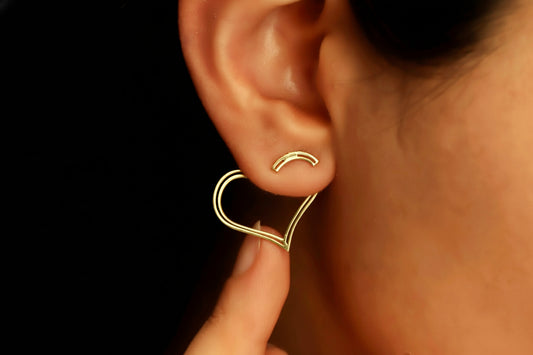 Gold heart-shaped earring being worn on an ear with a blurred background