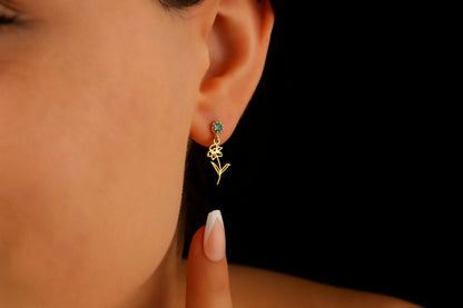 A close-up image of a woman's ear wearing a dangle birth month flower earring with a birthstone.
