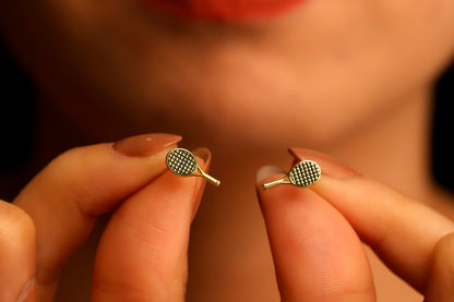 A close-up image of a gold tennis racket stud earring.