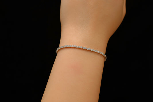 Silver tennis bracelet on a person's wrist against a black background