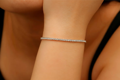 A close-up image of a person's wrist wearing a dainty tennis bracelet with gold filled detailing and small, possibly diamond-like stones.
