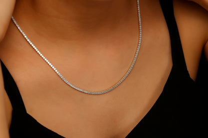 Silver diamond necklace on a person wearing a black top against a dark background