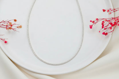 Silver diamond necklace on a white plate with red flowers