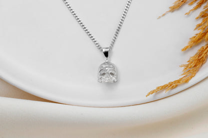 A close-up image of a minimalist skull charm necklace with a silver chain and a small skull pendant.