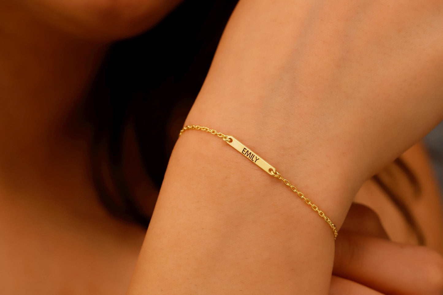 Gold bracelet with engraved name on a wrist against a neutral background