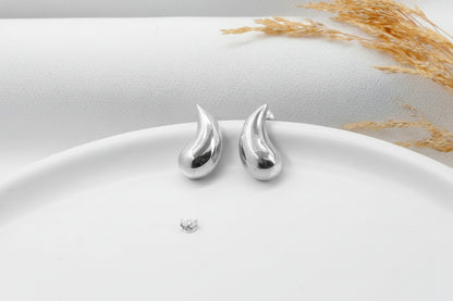 Silver teardrop-shaped earrings on a white plate with a light background