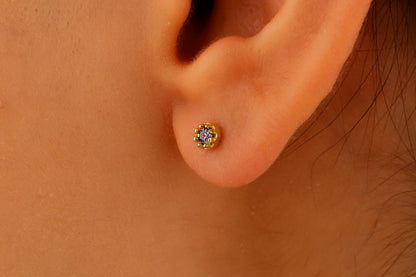 A close-up image of a person's ear wearing a small stud earring, with the focus on the earring and the soft earlobe.