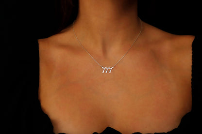 A close-up image of a necklace with the number '777' on a charm, held by a person with red nail polish.