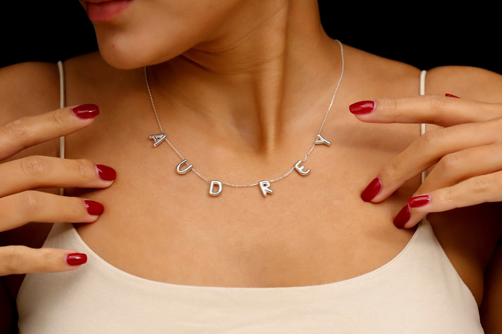 Necklace with 'AUDREY' pendant worn by a person with red nail polish.