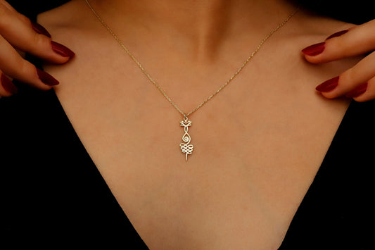 Gold necklace with a leaf pendant on a person's neck against a black background
