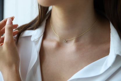 A woman wearing a white shirt touching her necklace, which is a 14K solid gold choker with an initial letter pendant.