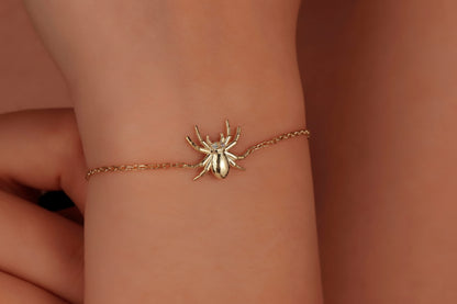 A gold-colored bracelet featuring a realistic spider design on a chain, displayed on a person's wrist.